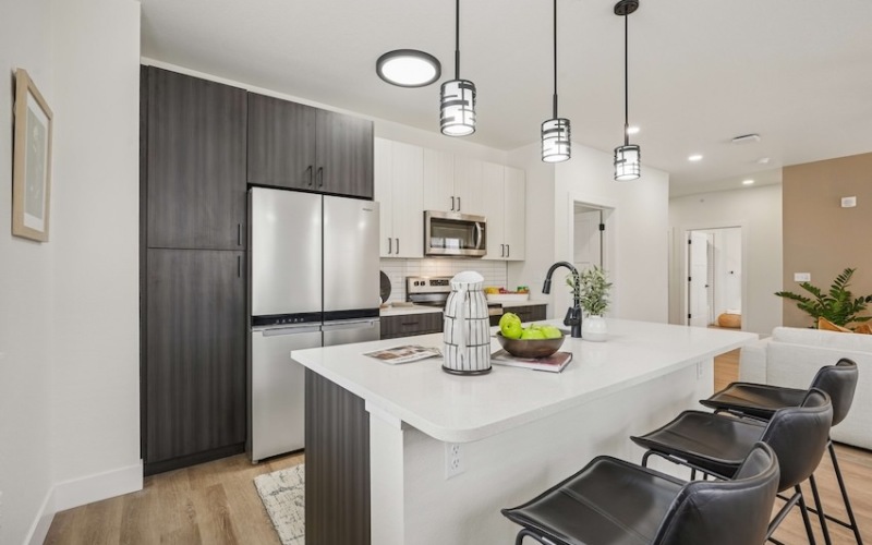  A modern kitchen with a white island and black chairs.